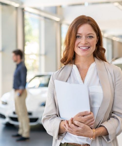 satisfied-saleswoman-in-car-dealership-DUKB7JX.jpg
